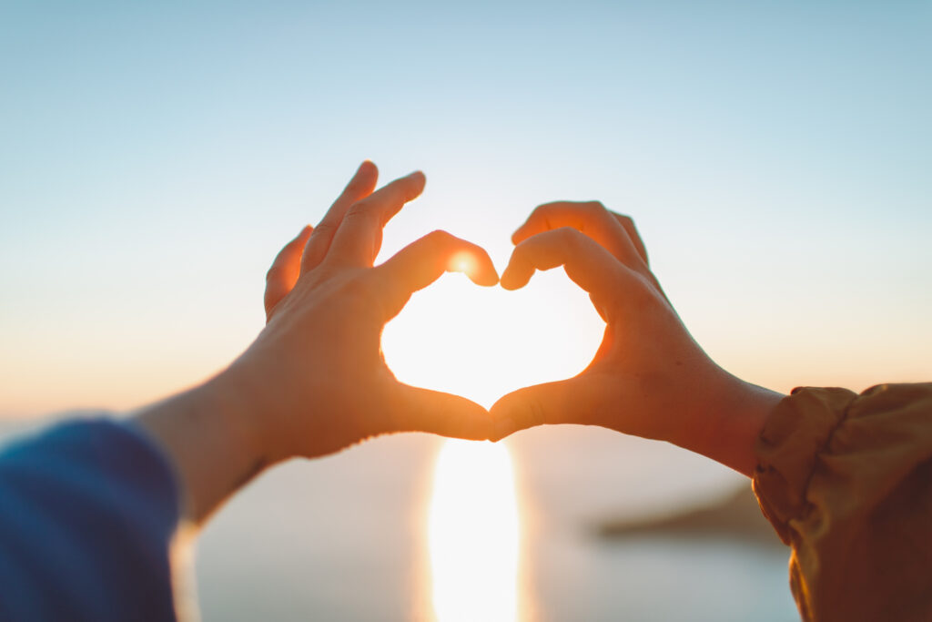 Two female friends making heart shape of hands at sunset at the sea